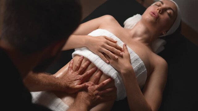 In a wellness session, a massage therapist presses and releases abdominal tissue with a measured therapeutic rhythm. The hands close view highlights tissue mobility, holistic wellness and client care.