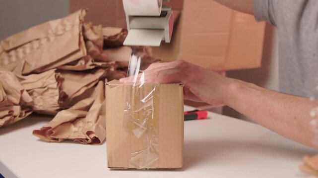 Man packs swiftly. Worker rapidly assembling and sealing packages at busy station. Energetic individual quickly folding and locking tabs on cardboard boxes for shipping
