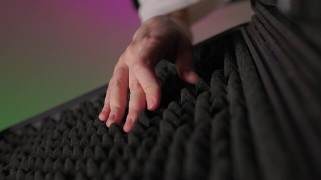 Mixer adjusting nearby. Adjusting audio mixer amid soundproofing in studio environment. Focus on live recording setup with tactile controls and soundproofing in studio setting