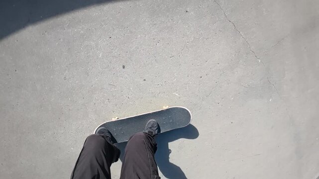 A skateboarder is doing a trick from a POV and slow motion in a skatepark on a sunny day