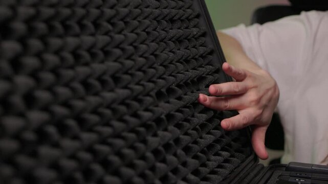 Hand touching foam rubber soundproofing panel, closeup texture study with soft studio light and eggcrate pattern conveying tactile curiosity and acoustic control