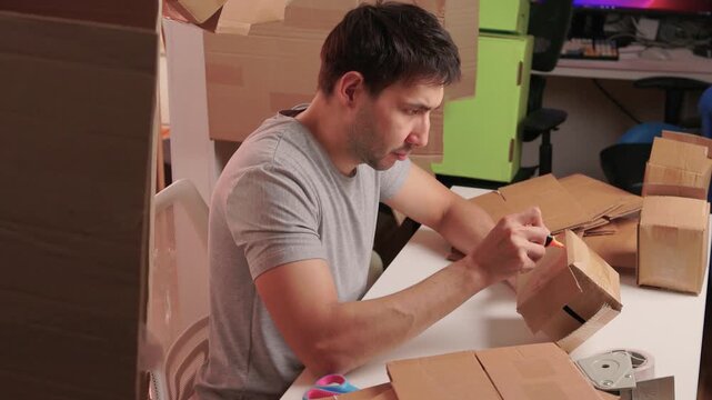 Man packs swiftly. Worker rapidly assembling and sealing packages at busy station. Energetic individual quickly folding and locking tabs on cardboard boxes for shipping