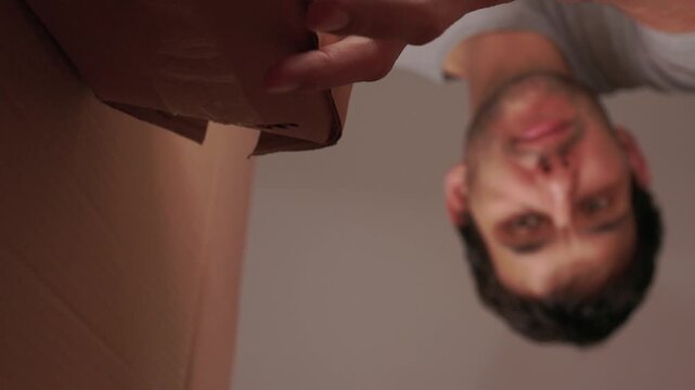 Man examines top of package carefully. Person inspects cardboard container from above cautiously. Individual looks over box from above with hesitant smile and care