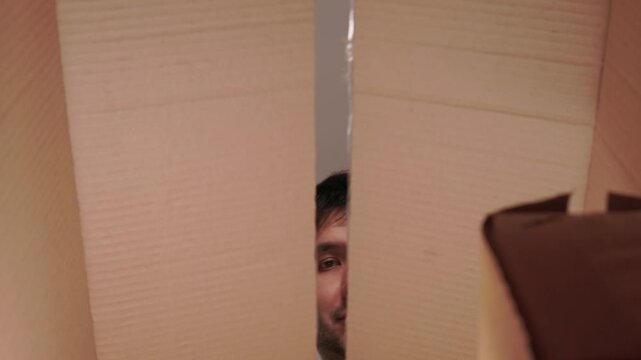 Man examines top of package carefully. Person inspects cardboard container from above cautiously. Individual looks over box from above with hesitant smile and care