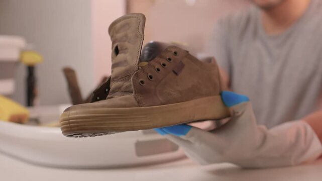 Gloved hands scrubbing suede boots, closeup of sponge lathering dirt and salt stains, patient circular motions, basin with foam, warm indoor lighting, home care scene