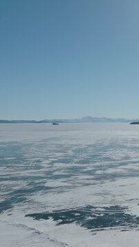 Aerial winter landscape of the frozen Maloye More strait on Lake Baikal, Russia, with vast ice fields, cracks and snow patterns under clear blue sky