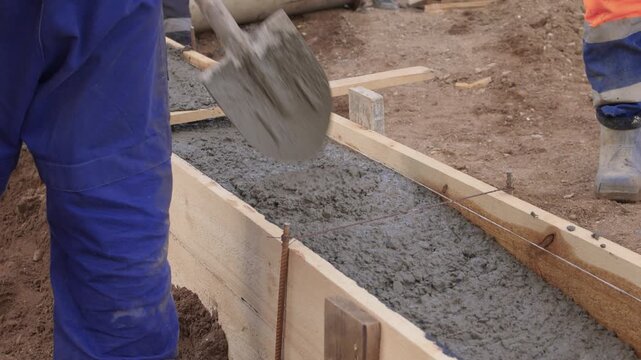 Construction worker actively pouring concrete into forms. Construction worker skillfully pouring wet concrete into formwork amid surrounding earth and safety gear