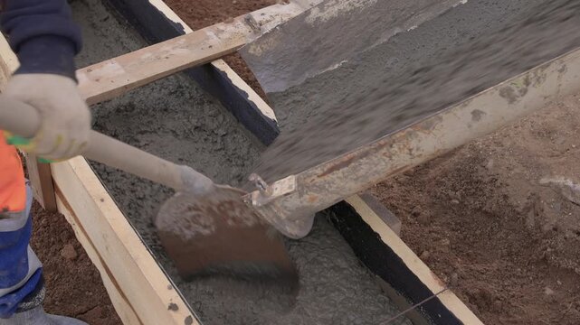 Construction worker actively pouring concrete into forms. Construction worker skillfully pouring wet concrete into formwork amid surrounding earth and safety gear