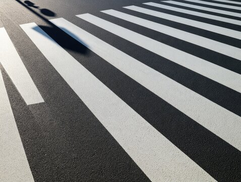 Black and white striped crosswalk on asphalt, casting a long shadow