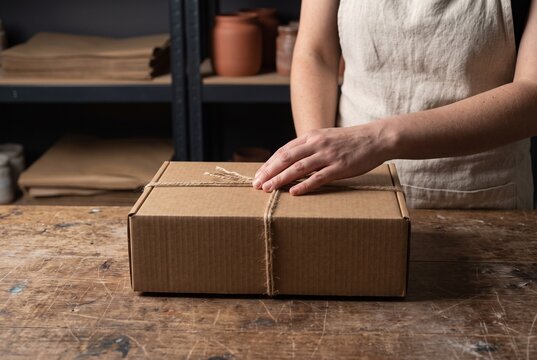 Female artisan packing a cardboard parcel tied with twine string on a wooden table in a workshop
