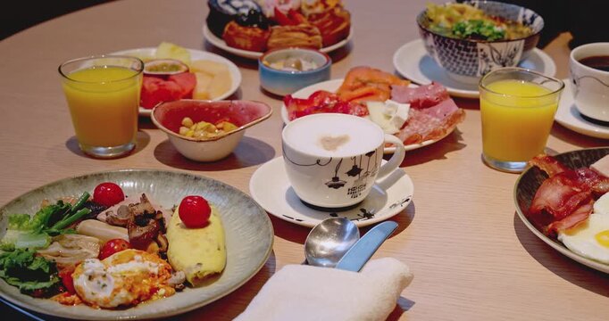 Breakfast buffet spread on wooden table. Includes coffee, orange juice, omelet, fruit, and cold cuts. Morning dining in hotel restaurant. High angle close-up view.