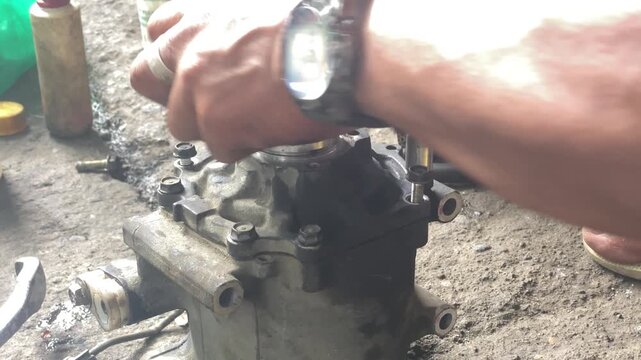 technician is assembling pieces of a broken car air conditioning compressor on the pavement.