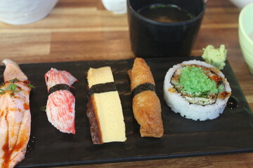 Tamago egg sushi, inari tofu sushi and a sushi roll with wasabi on a black plate © 유진 김