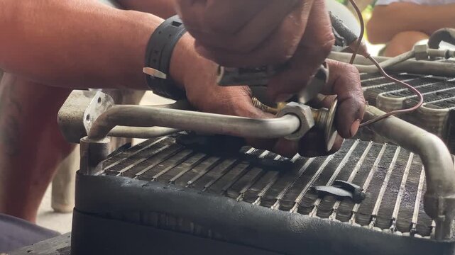 technician is assembling pieces of a broken car air conditioning evaporator on the pavement.