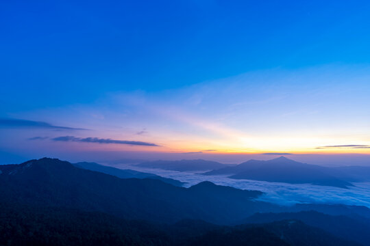 Blue hour sky above layered mountains and a sea of clouds with colorful sunrise and sunset glow