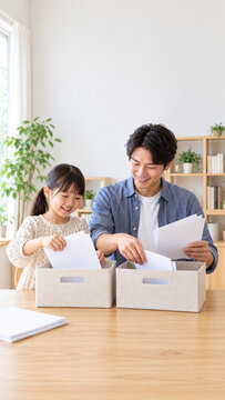 Father and daughter sorting papers into storage boxes at home，自宅で紙を収納ボックスに整理する父と娘