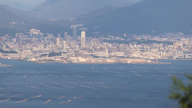 Hiroshima City aerial panoramic view seen from Mount Misen on Miyajima Island, with Seto Inland Sea, Hiroshuma bay and skyline, port and oyster farming rafts, Chugoku, Japan, mountains in background