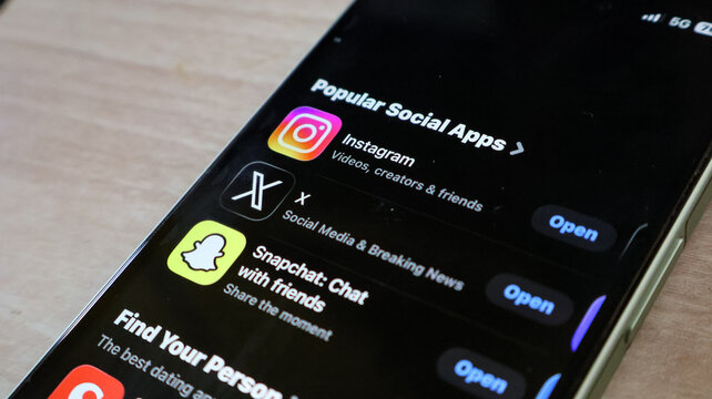 A close-up view of an iphone display showing popular social apps with black background against a wooden table.
