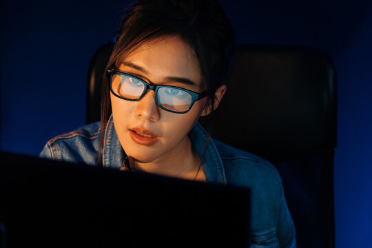 Portrait young beautiful Asian creative with glasses of serious face looking on pc to search project creator social media online, planning strategy creator at neon modern office at night. Stratagem.