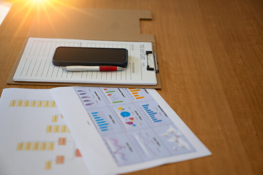 Smartphone and pen placed on a clipboard with a to-do list beside printed business charts and reports, representing productivity, task management, business planning and office organization.