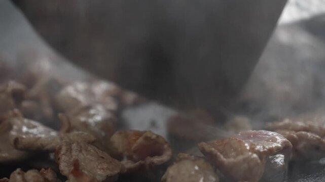 cinematic close-up shot of juicy meat pieces sizzling on a hot flat iron griddle with smoke rising and a metal spatula turning the food