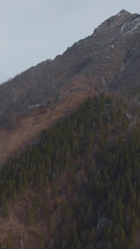 Aerial footage of Love Peak mountain ridge with conifer forest and snowy slopes near Arshan village, Republic of Buryatia, Russia, dramatic wilderness landscape