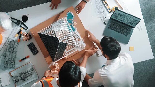 Top view of skilled architect designer team using pencil measuring house model. Group of civil engineer planning and designing blueprint while pointing at building at table with laptop. Alimentation.