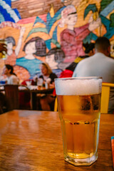 A cold glass of beer on a rustic wooden table in a vibrant restaurant setting, ideal for menu design. © garcon daily photo