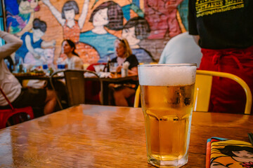 Frothy beer in a glass on a wooden table, with a colorful coaster and blurred restaurant background, suitable for advertisements. © garcon daily photo