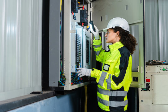 Female electrician inspecting electrical panel and circuit breakers during maintenance at industrial plant, industrial worker managing power distribution