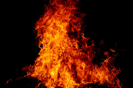 Glowing flame above charred wood. Flame pattern against black. Swirling flame with burning wood. Flame background with intense heat.