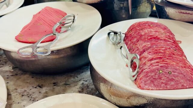Macro shot of sliced salami sausage and smoked meat on hotel buffet plates. Gourmet cold cuts close up served for breakfast catering at luxury all inclusive resort restaurant. Food video.
