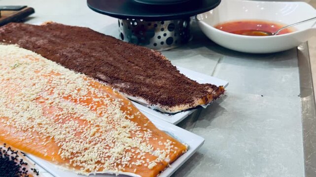 Four salted salmon fillet pieces with black sesame seeds and different spices on plates at resort buffet counter. Five stars hotel restaurant dining area background, cold fish appetizers photo