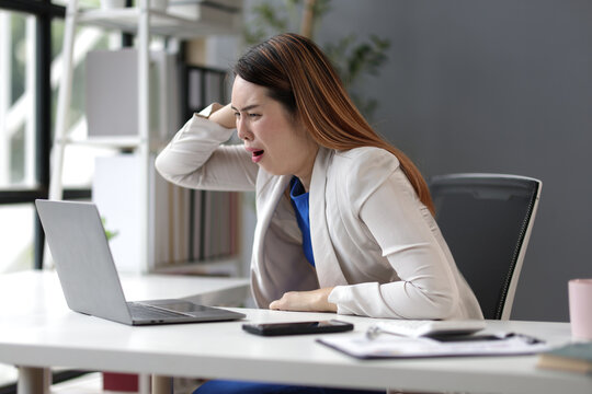 Stressed businesswoman is holding her head with her hands while working with a tablet in the office, experiencing frustration and burnout from excessive workload and pressure.