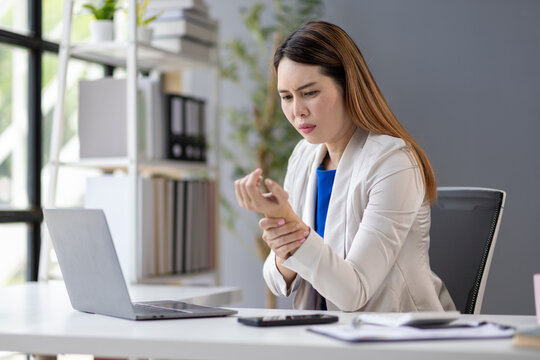 Businesswoman suffering wrist pain while working on laptop in office.