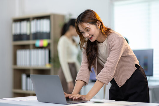 Asian businesswoman is smiling and working using laptop computer at her desk in a modern office.