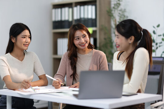 Group of young businesswomen discussing work at office desk.
