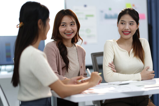 Group of young businesswomen discussing work at office desk.