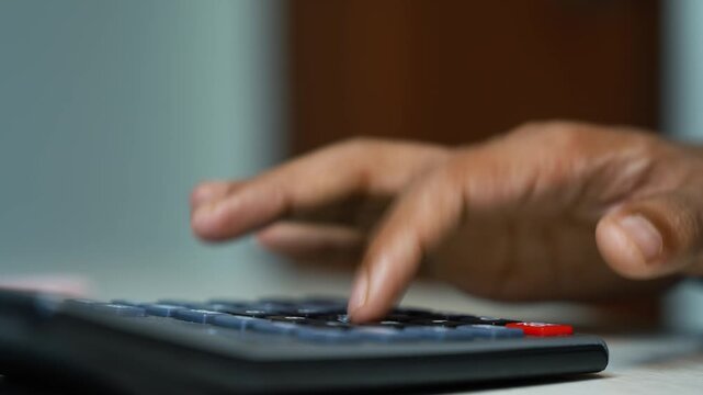Hand using calculator for budget planning, Close-up of a hand pressing a calculator on a desk, with shallow focus and a red button in view. Useful for finance, budgeting, accounting, tax.