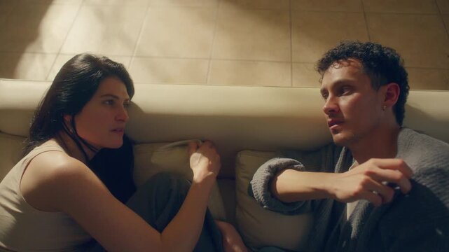 Young couple sitting on couch at home, talking calmly as trying to reconcile and resolve relationship problem after argument. High angle view