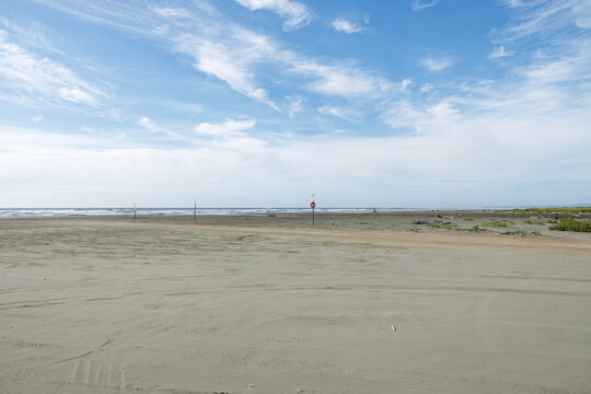 Empty wide sandy beach at Copalis Beach, Washington, with distant surf, marker posts and a red Do Not Enter sign beneath a bright blue sky and wispy clouds.