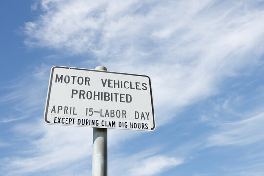 Motor vehicles prohibited sign, April 15 to Labor Day except during clam dig hours, on a metal pole against a blue sky with cirrus clouds at Copalis Beach, Washington.