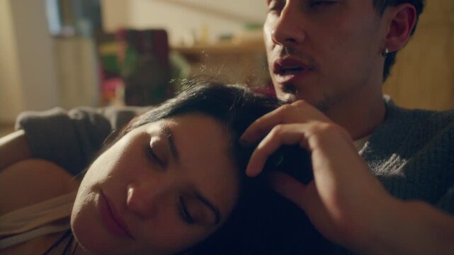 Caring young man affectionately stroking his partners dark hair as she resting her head on his chest during intimate conversation on sofa after reconciliation at home. Close up shot