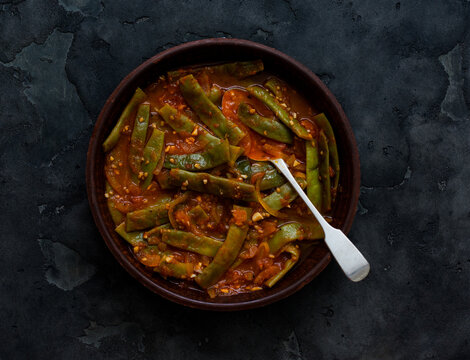 Stewed green string beans in tomato sauce against a dark background, top view