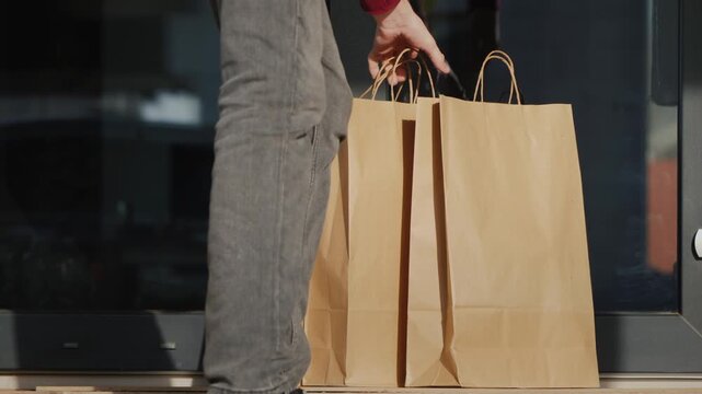 Delivery person places brown paper shopping bags near modern building glass door.