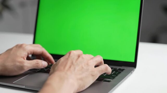 Male hands of a programmer or office worker typing on a modern laptop keyboard with a green screen for custom content insertion