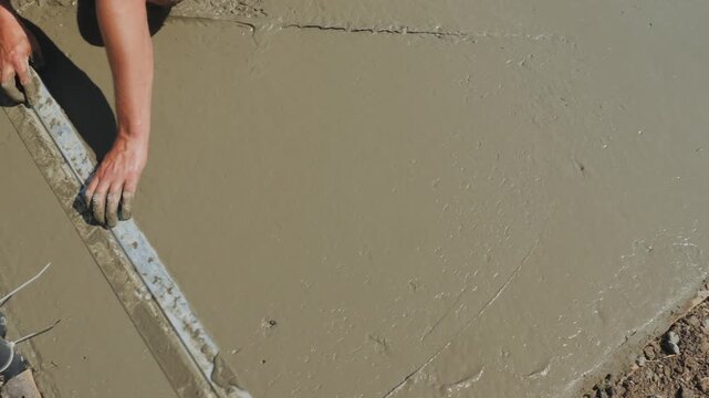 Worker using aluminum level tool to smooth wet concrete surface during construction project.