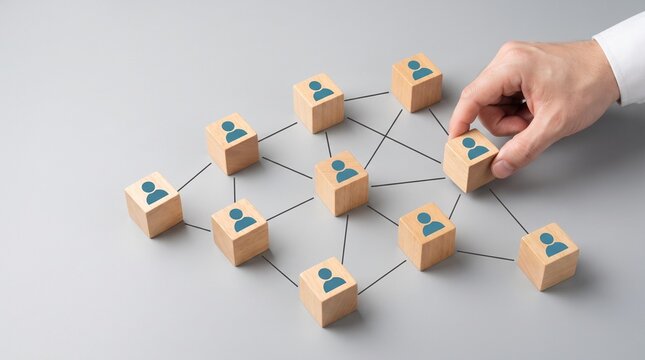 Human resources and team structure concept photo. Businessman hand organizing wooden cubes with person icons connected by lines. Corporate management, networking, and talent acquisition.