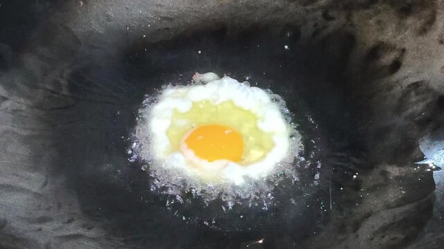 Sunny-side-up fried egg prepared as a topping for Indonesian fried noodles, featuring a golden crispy edge, cooked egg white, and soft yolk, commonly served by street food vendors