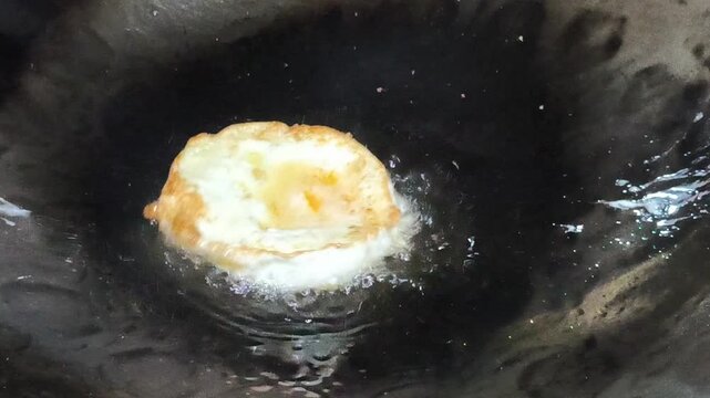 Sunny-side-up fried egg prepared as a topping for Indonesian fried noodles, featuring a golden crispy edge, cooked egg white, and soft yolk, commonly served by street food vendors